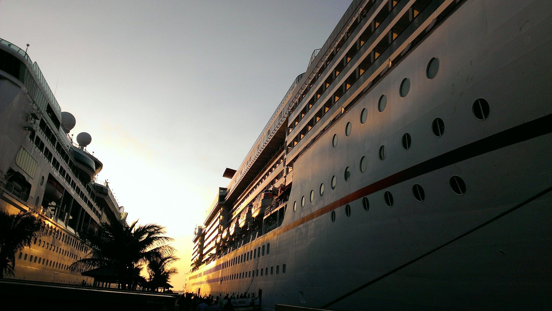 Royal Caribbean and Carnival cruise ships docked side by side in the Caribbean, with families walking along the pier