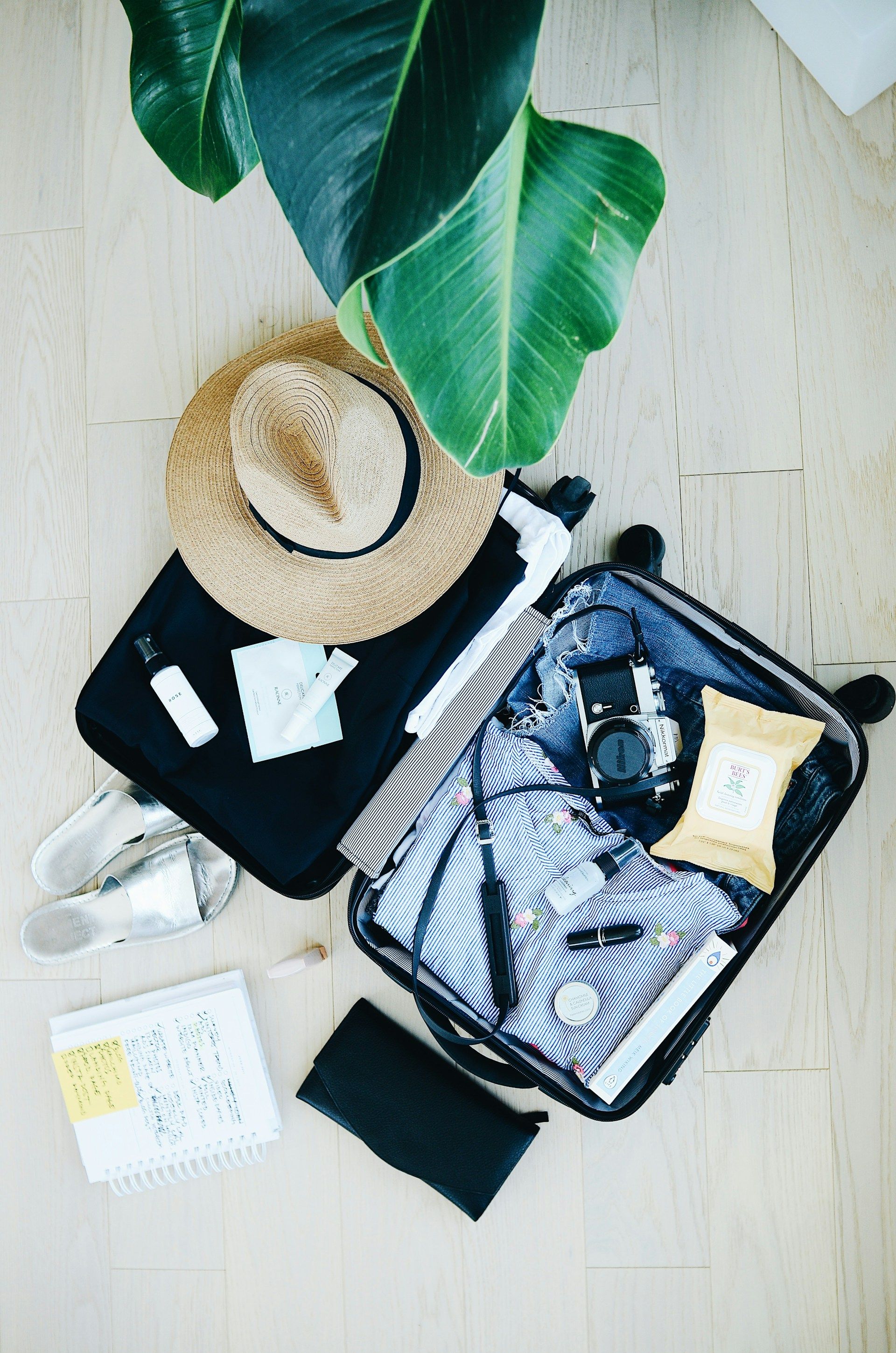 Open suitcase on a bed packed with cruise essentials for a Caribbean vacation, including swimsuits, sunhat, sandals, and travel-sized toiletries