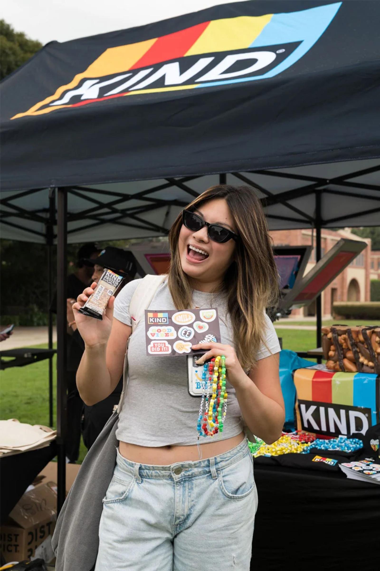 College student holding a KIND protein bar at a campus brand activation tent
