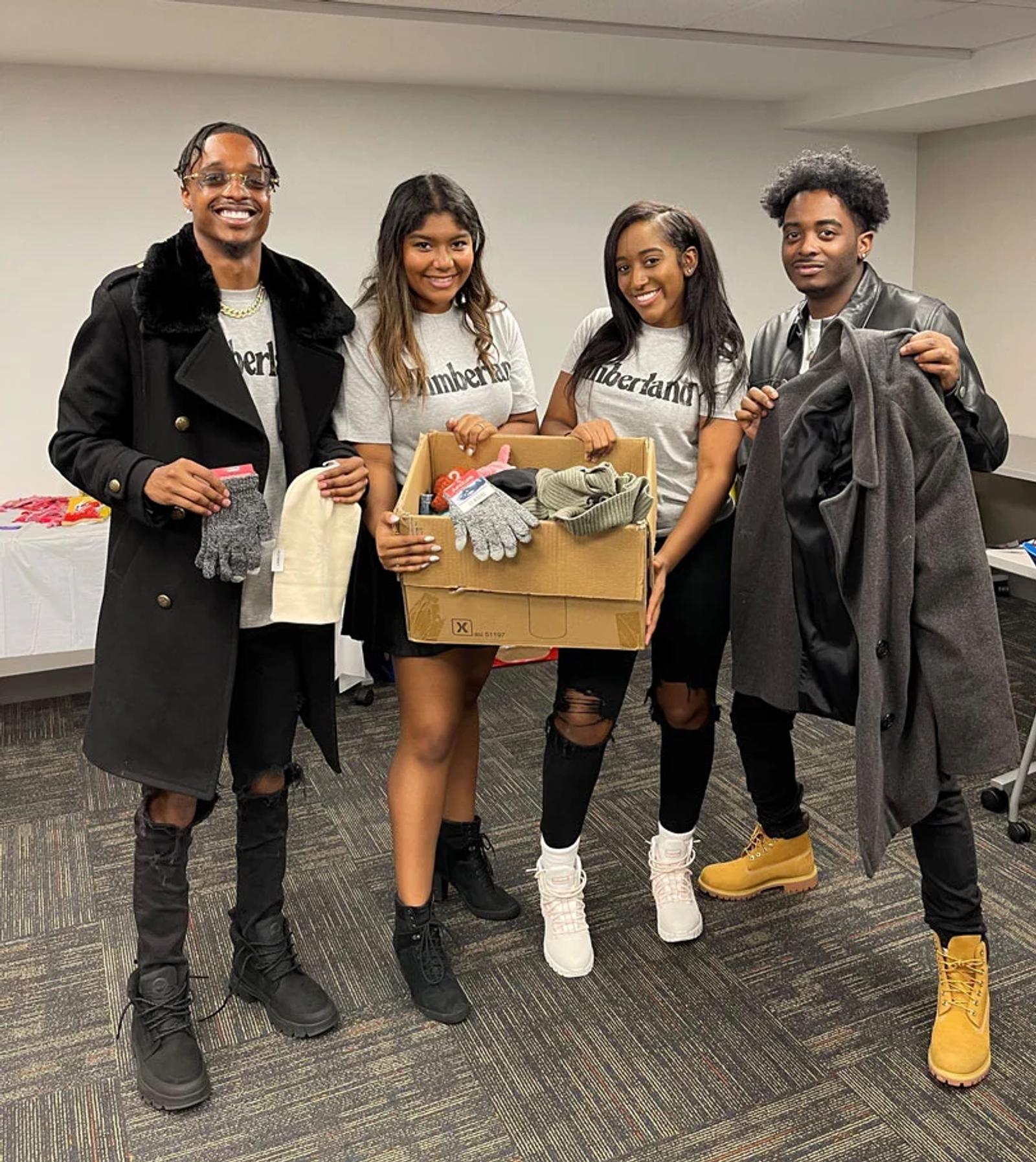 Image of four people in Timberland gear holding a box of gloves, hats, and a coat