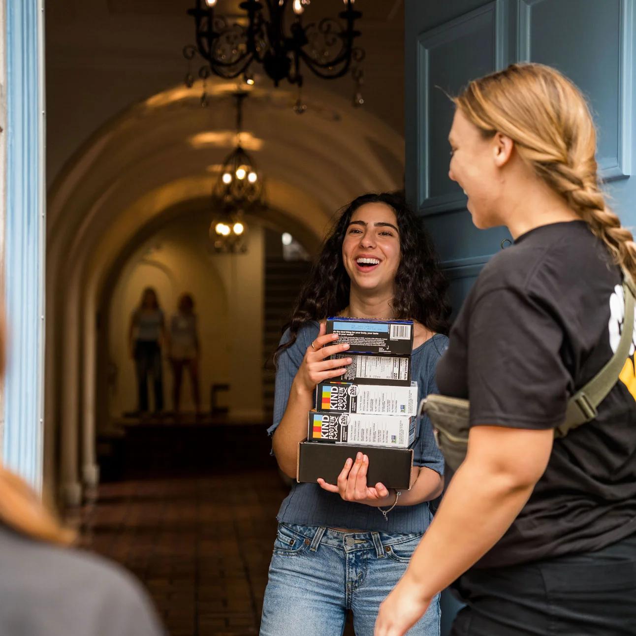 Image of a student laughing while receiving KIND protein bar boxes from a brand ambassador indoors