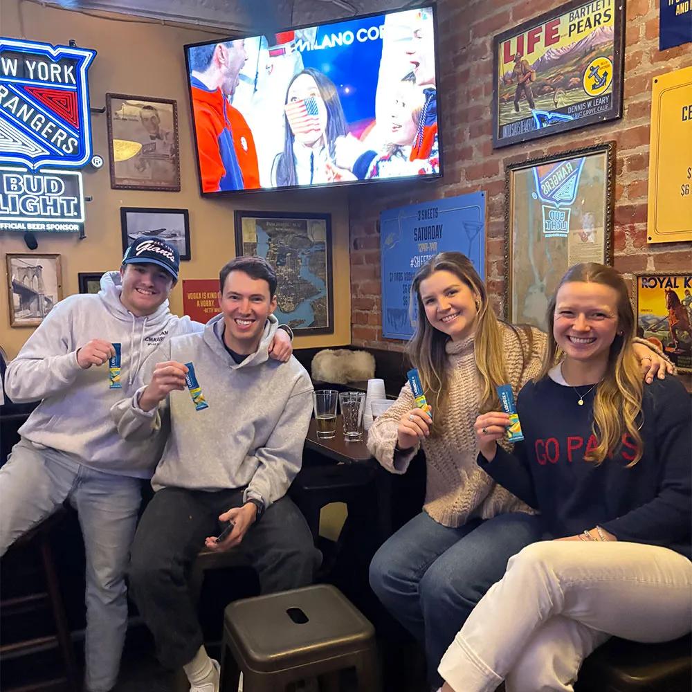 Image of four friends at a sports bar holding Liquid I.V. sample sticks during a product sampling activation