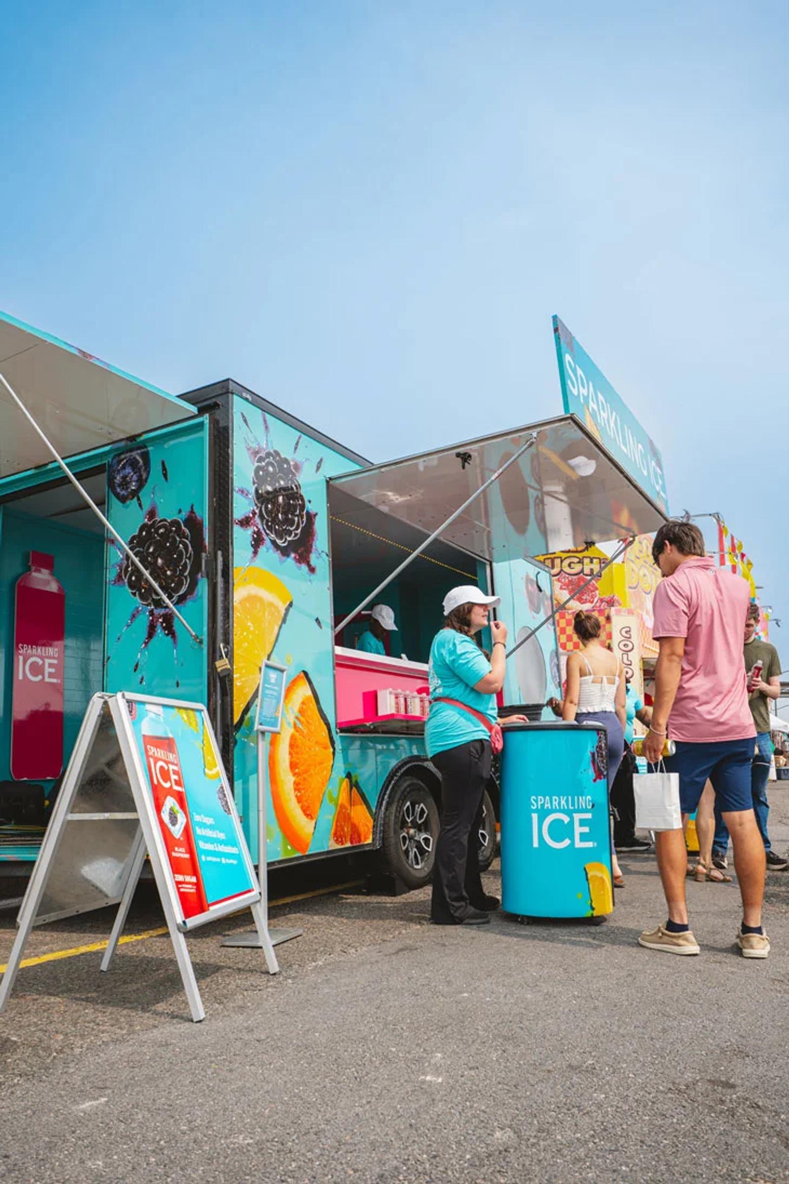 A Sparkling Ice promotional truck at an outdoor event, with a brand representative speaking to a visitor beside the colorful display