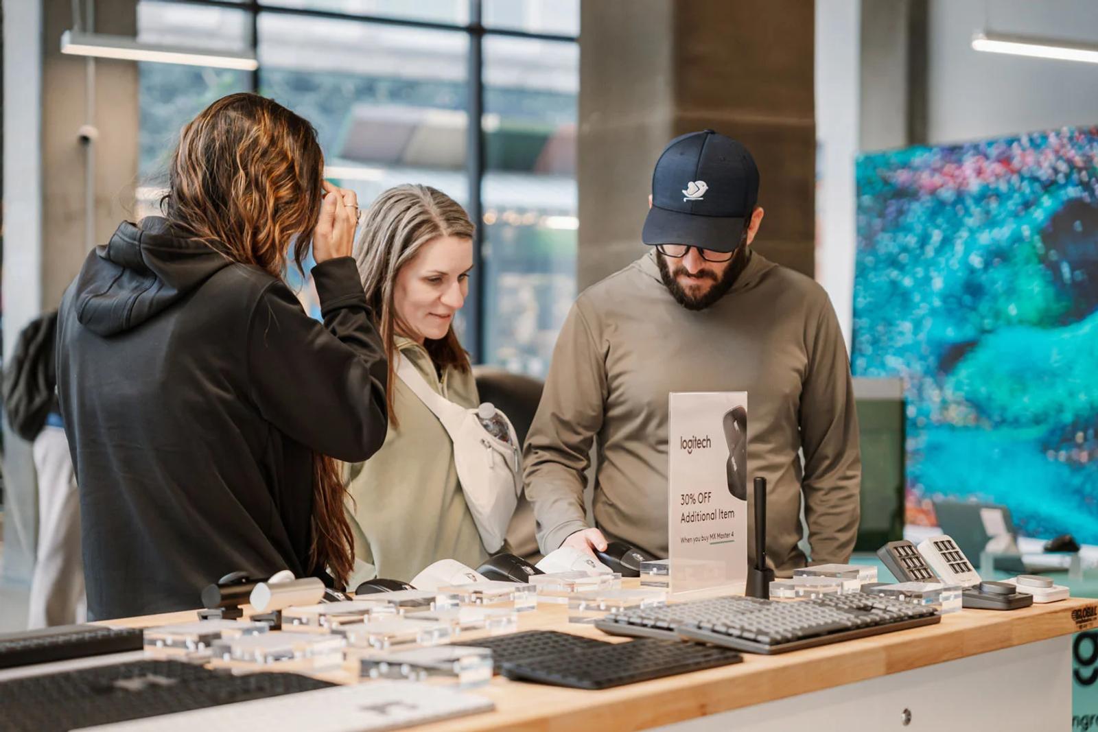 image of shoppers testing Logitech mice and keyboards at a retail product demo table with a 30% off promotion