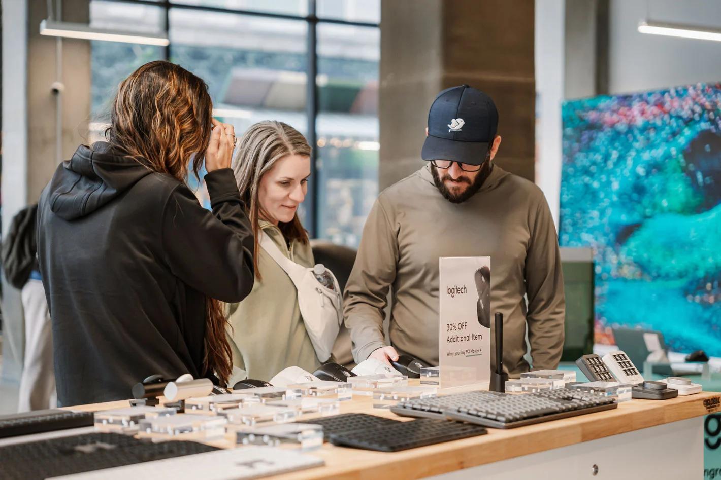 image of shoppers testing Logitech mice and keyboards at a retail product demo table with a 30% off promotion