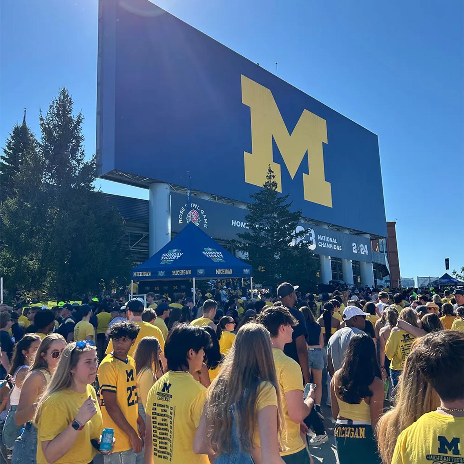 Image of a crowd of Michigan fans walking past the YouTube NFL Sunday Ticket tent outside Michigan Stadium
