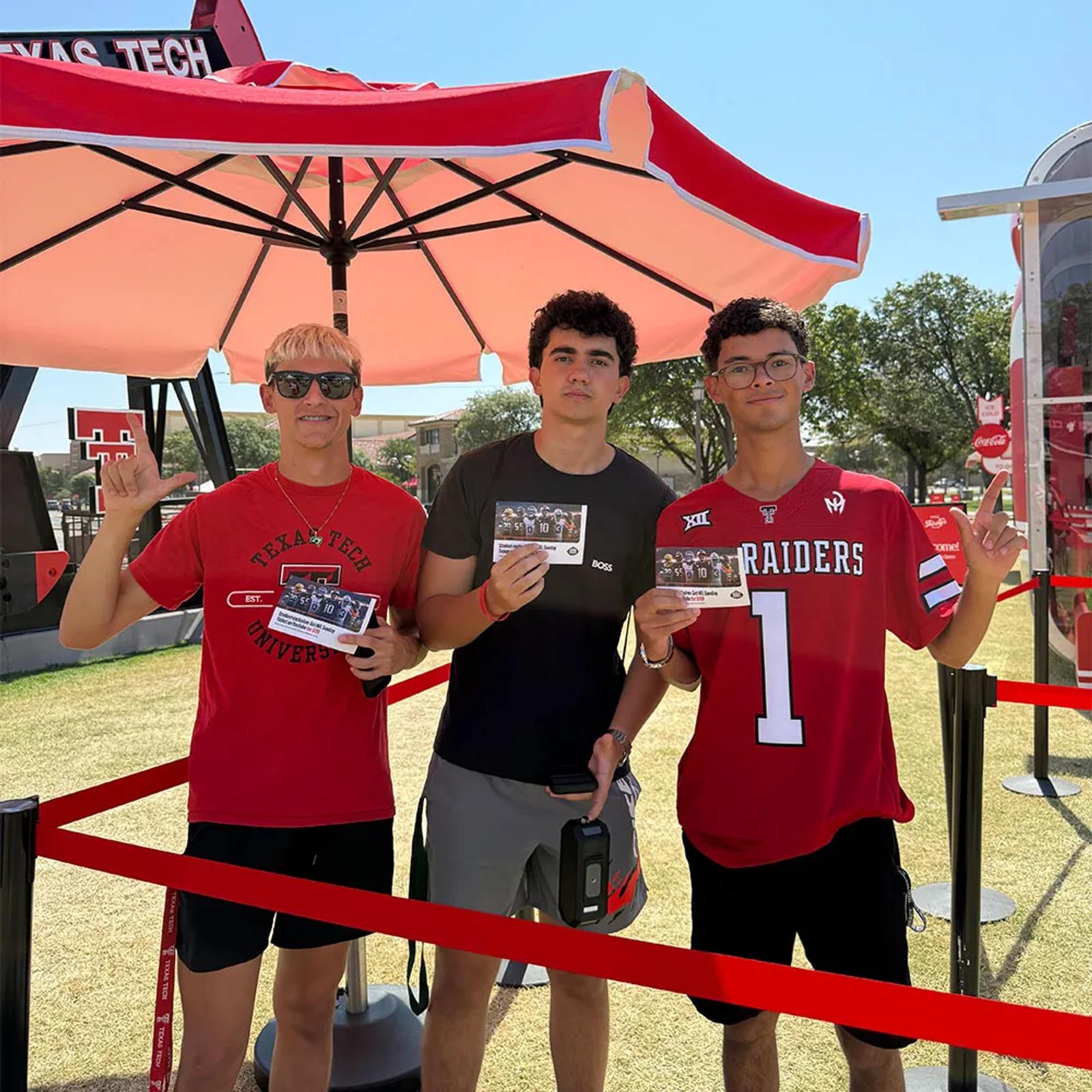 Image of three Texas Tech students holding YouTube NFL Sunday Ticket offer cards under a red umbrella