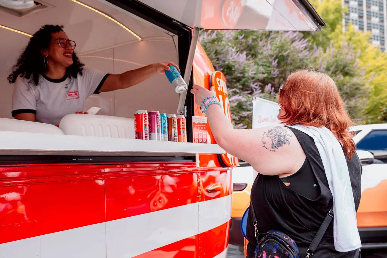 Image of a brand ambassador handing a canned beverage to an attendee at a CPG sampling truck