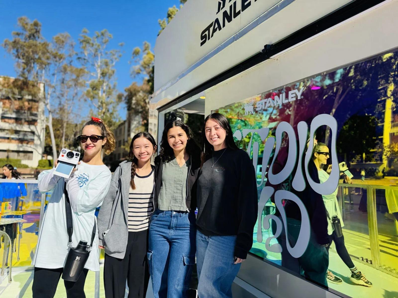 Image of four young women posing in front of a Stanley branded experiential marketing truck at an outdoor campus event