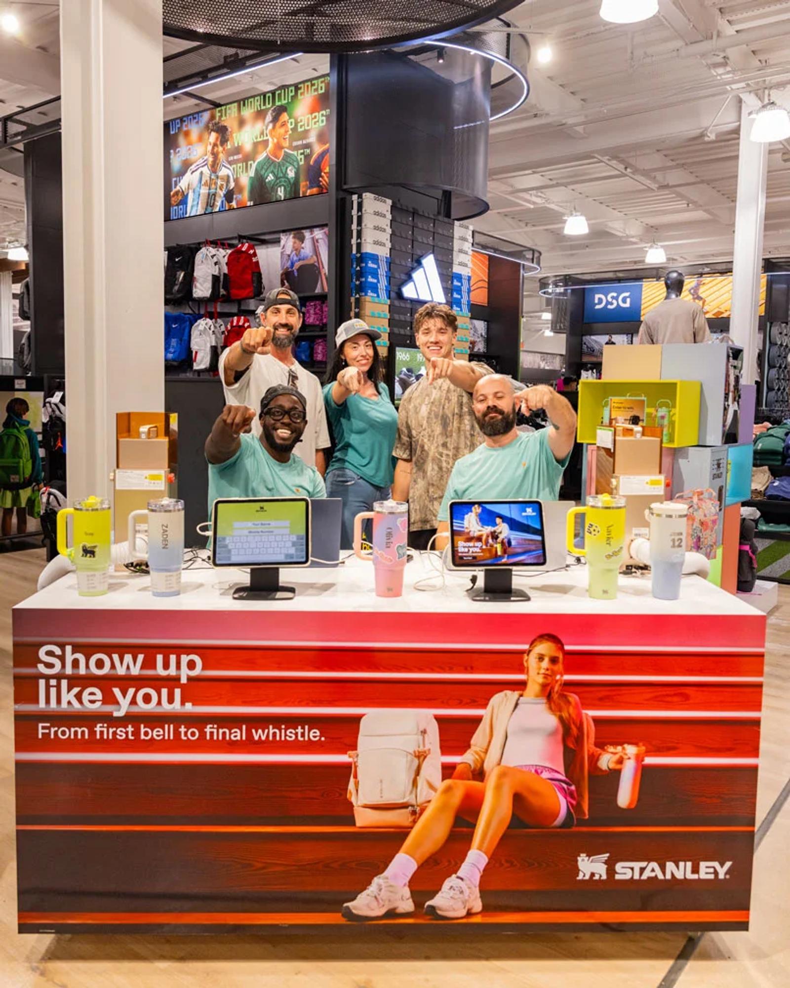 Image of a retail activation team engaging shoppers at a Stanley display table inside Dick's Sporting Goods