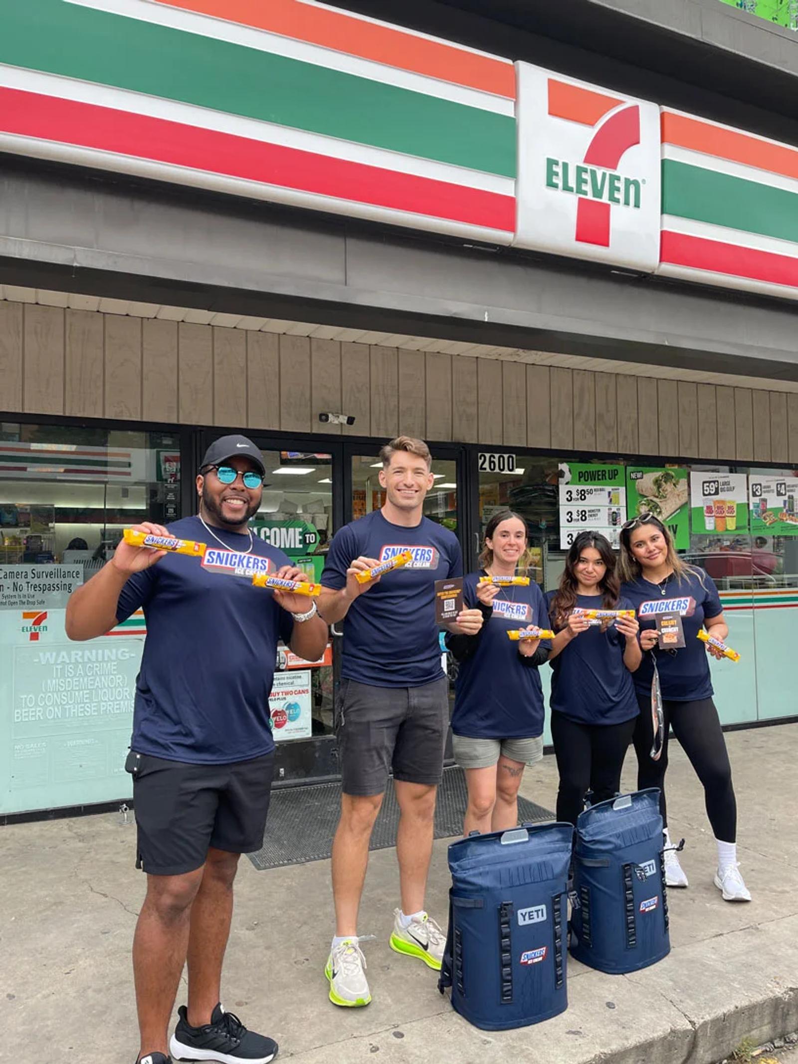 Image of a street team marketing crew sampling Snickers bars outside a 7-Eleven storefront
