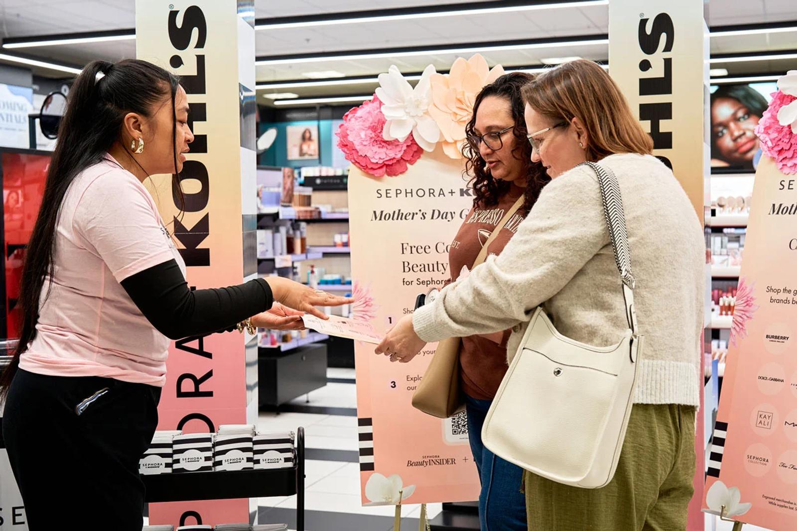 Image of Sephora associate handing a Mother's Day gift card to shoppers at a Kohl's retail counter in-store