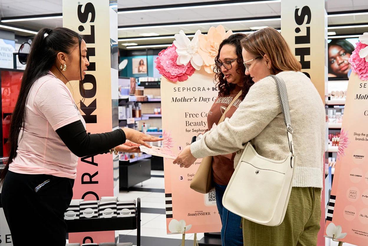 Image of Sephora associate handing a Mother's Day gift card to shoppers at a Kohl's retail counter in-store