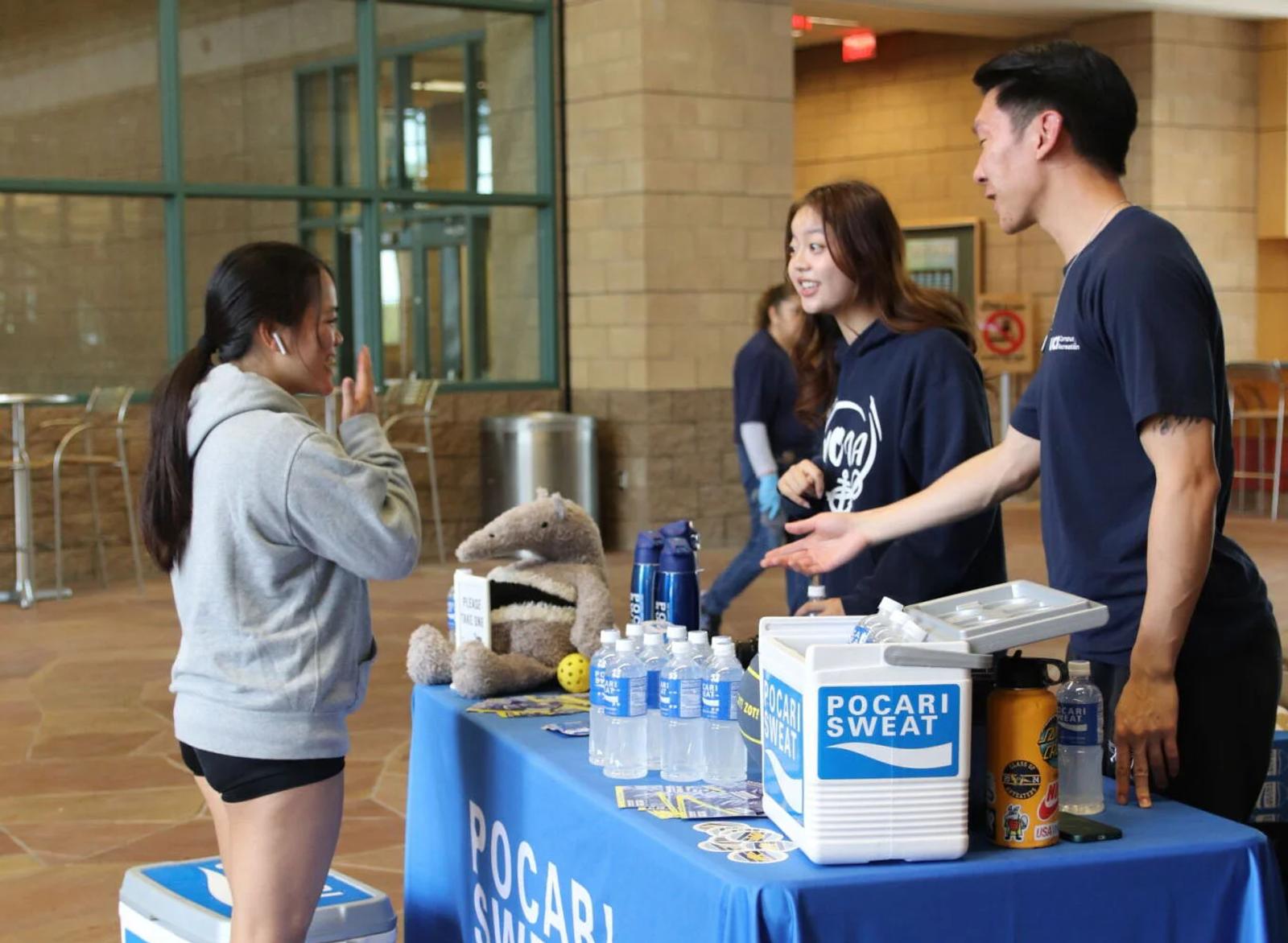 Image of Pocari Sweat brand ambassadors offering samples at a campus table, showing how brands use events to build loyalty