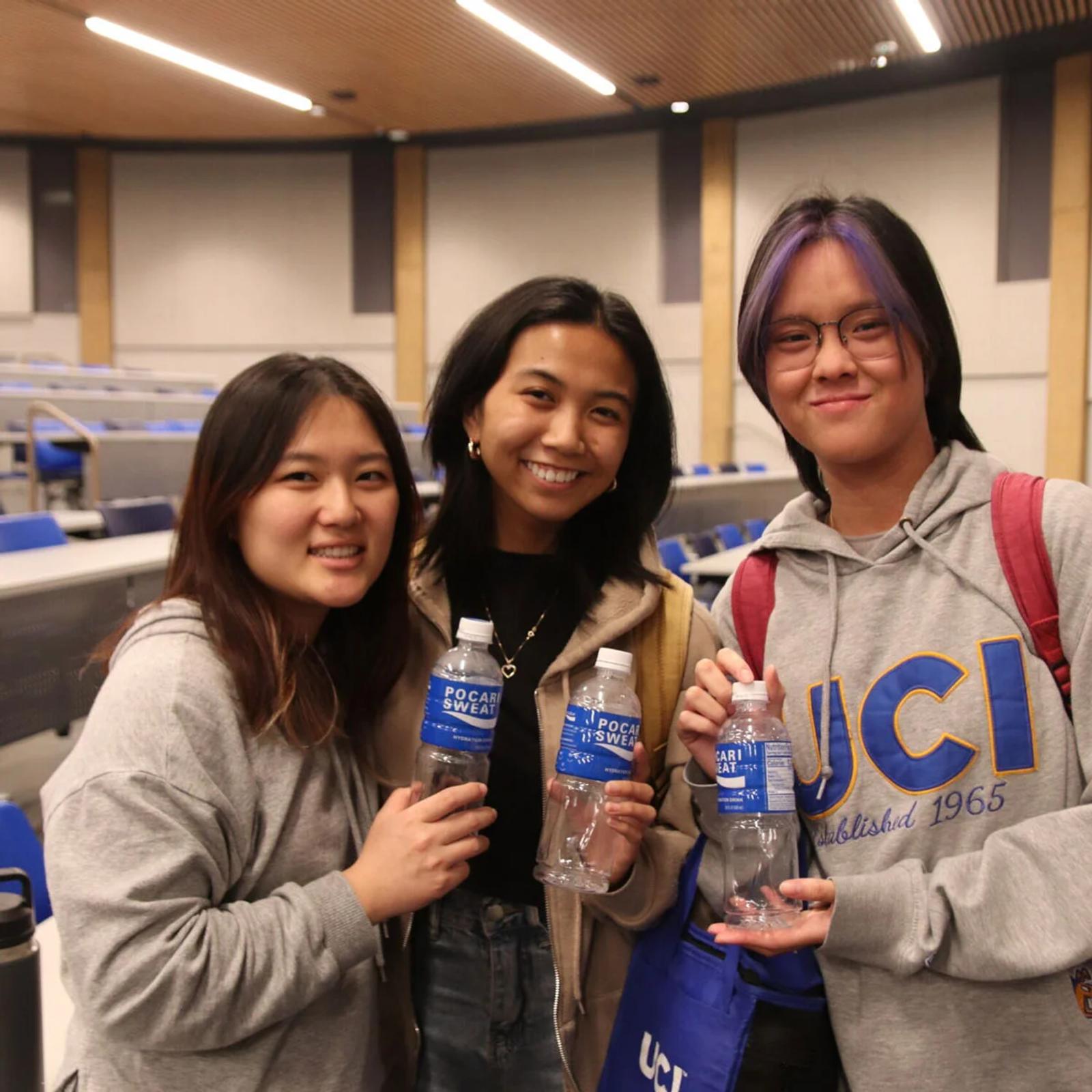 Photo three students holding water bottles in lecture hall