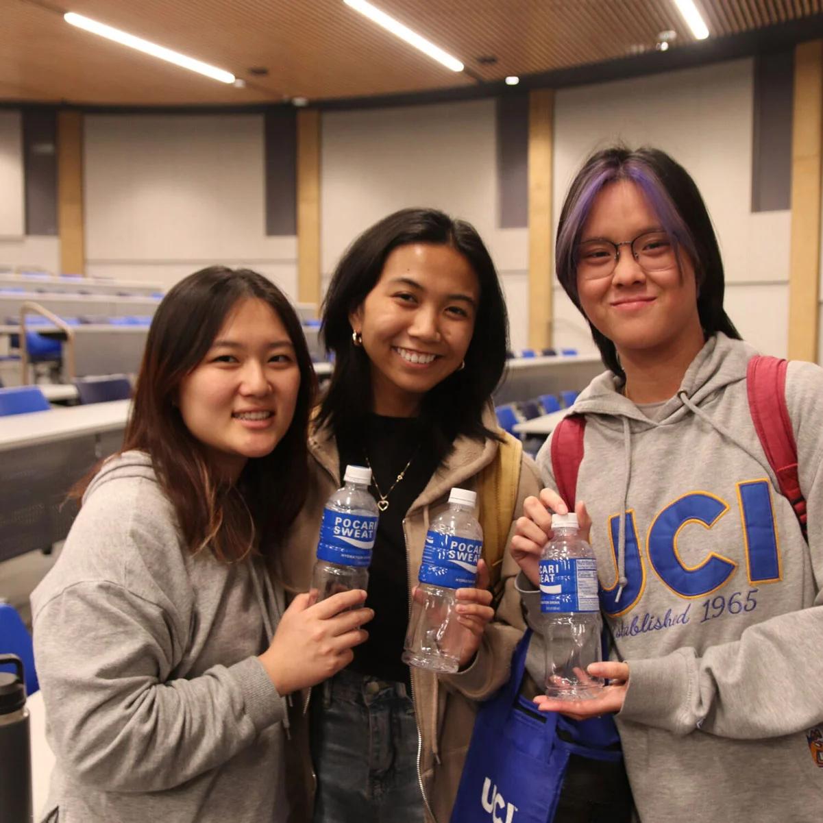 Photo three students holding water bottles in lecture hall