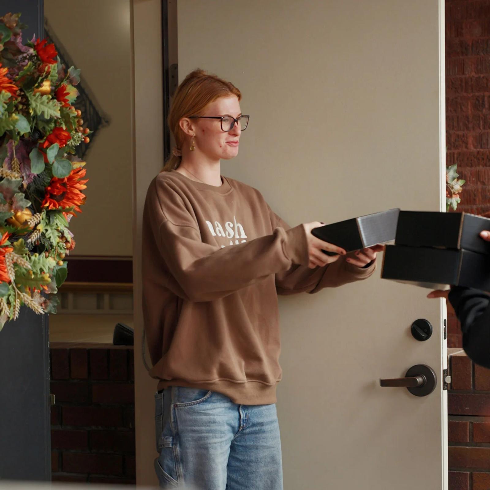 Image of a brand ambassador handing a KIND sample box to a student at a residence hall doorway