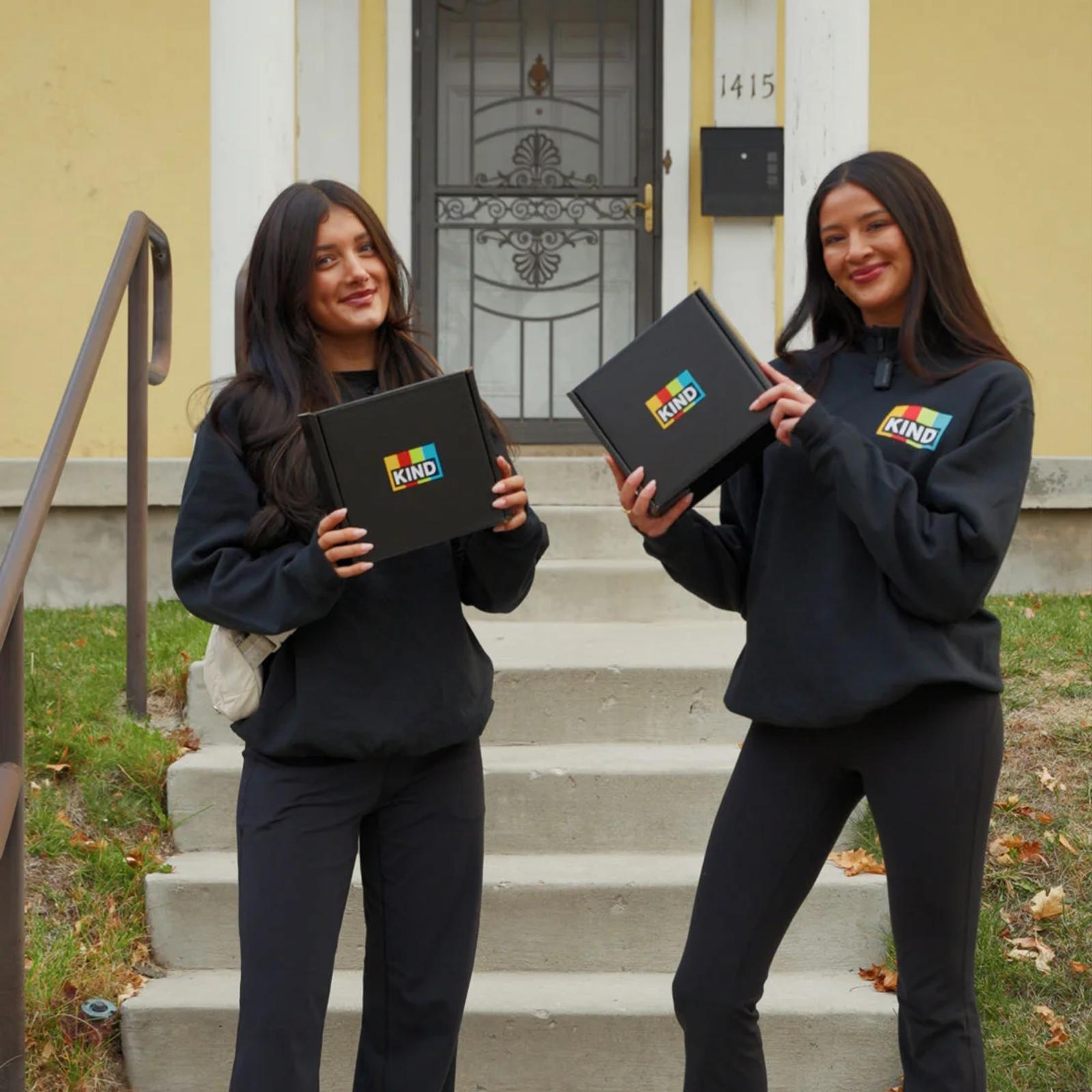 Image of two brand ambassadors holding KIND snack boxes on a house porch during a campus sampling activation