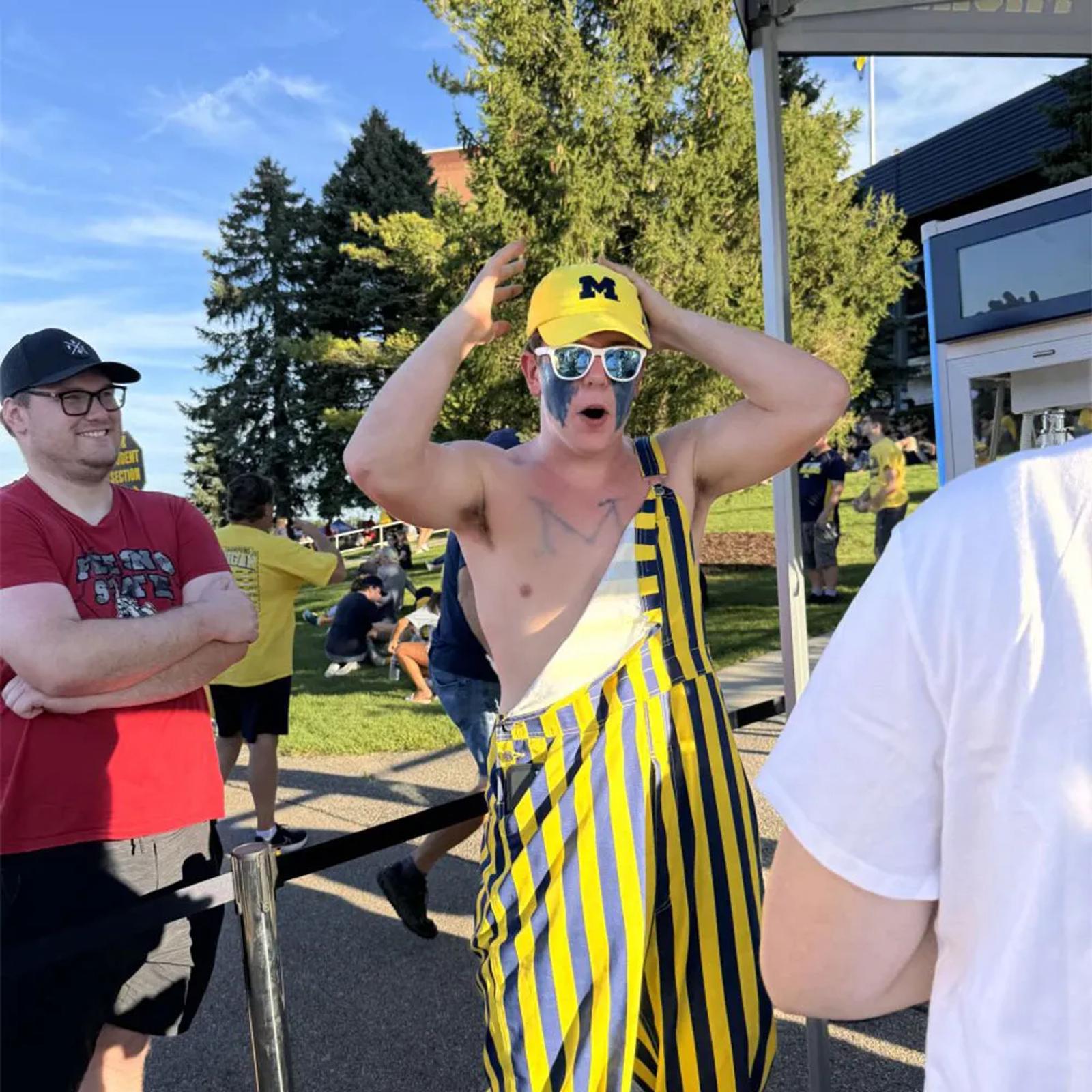 Image of a Michigan fan in striped overalls reacting in line at a YouTube NFL Sunday Ticket activation