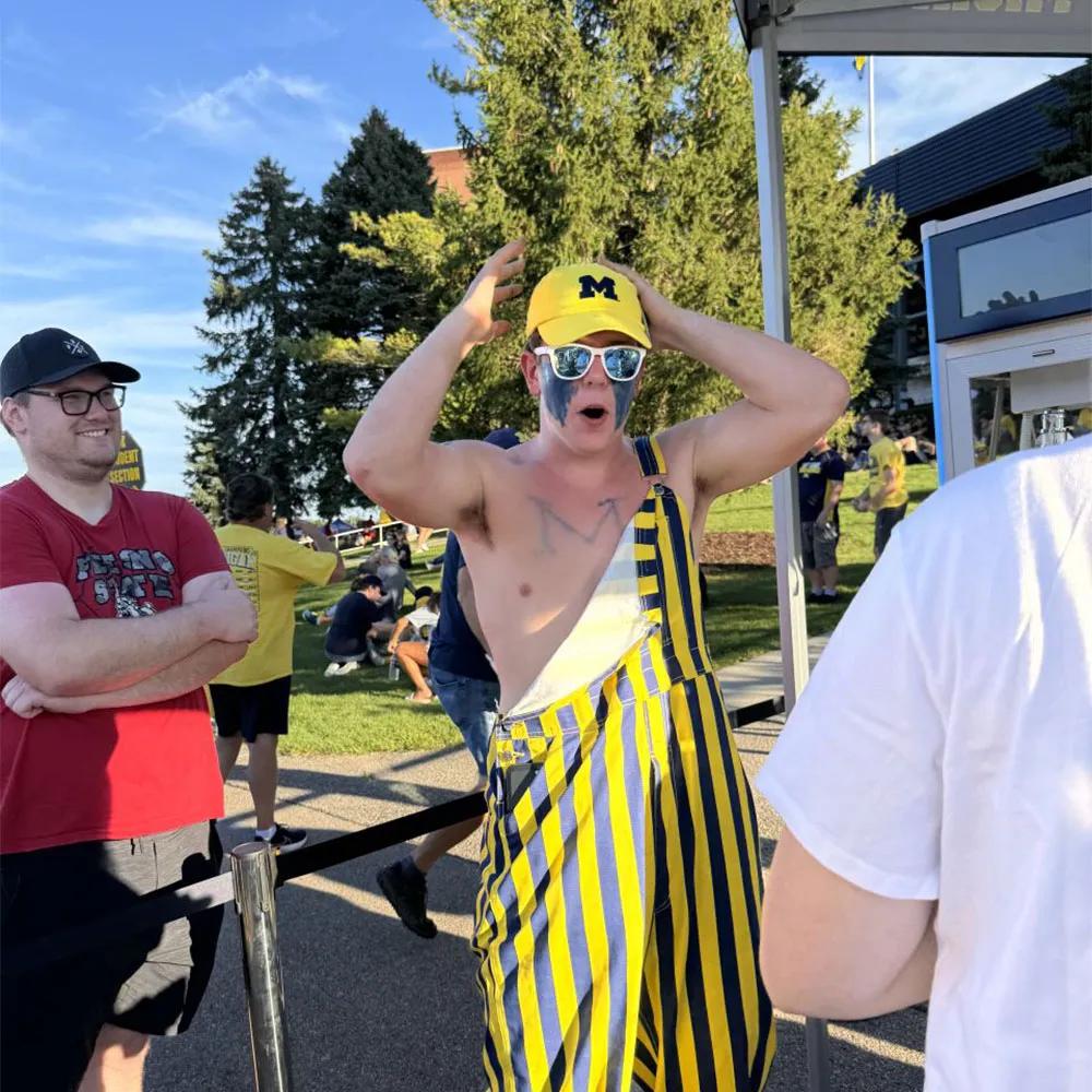 Image of a Michigan fan in striped overalls reacting in line at a YouTube NFL Sunday Ticket activation