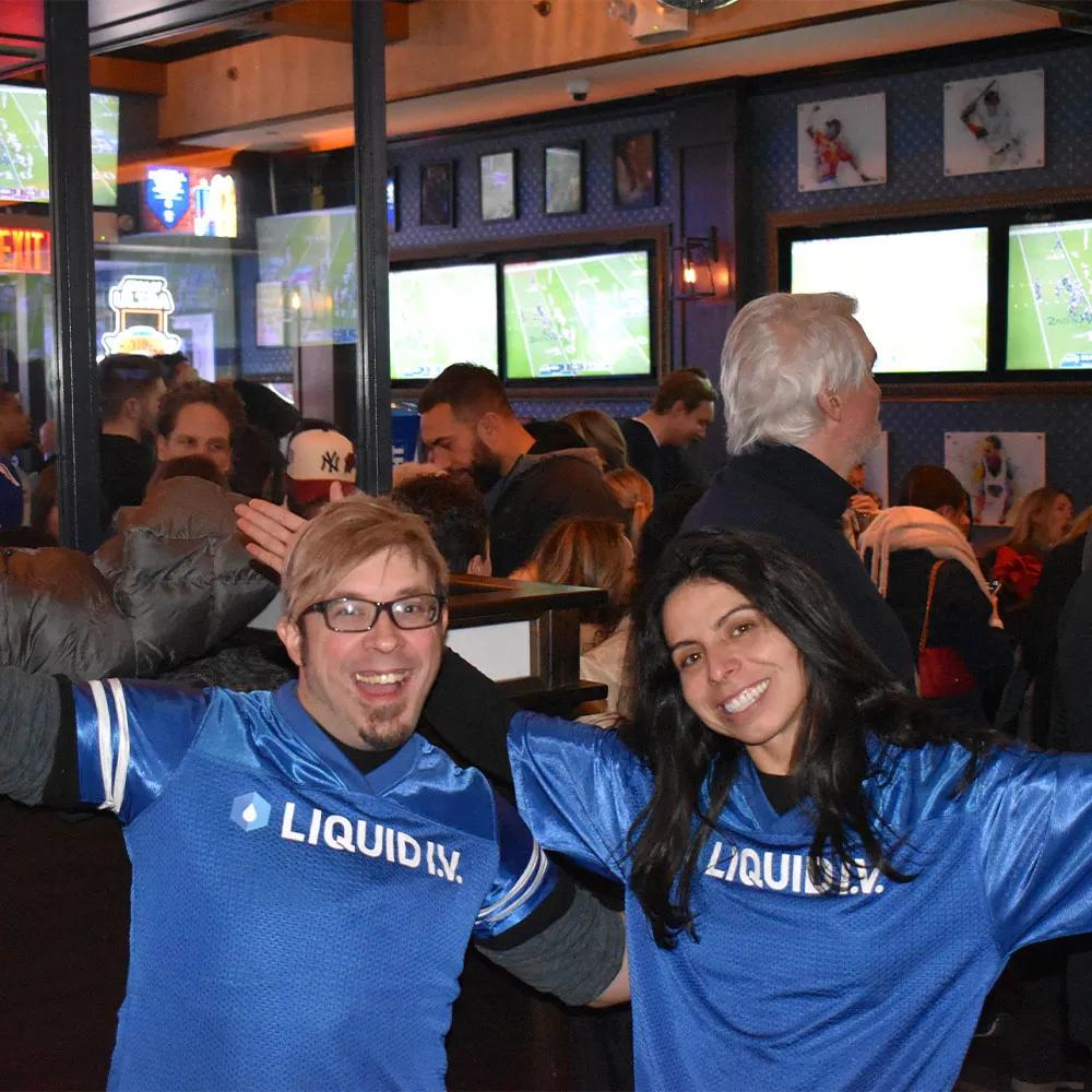 Image of two fans in Liquid I.V. football jerseys cheering at a sports bar watch party
