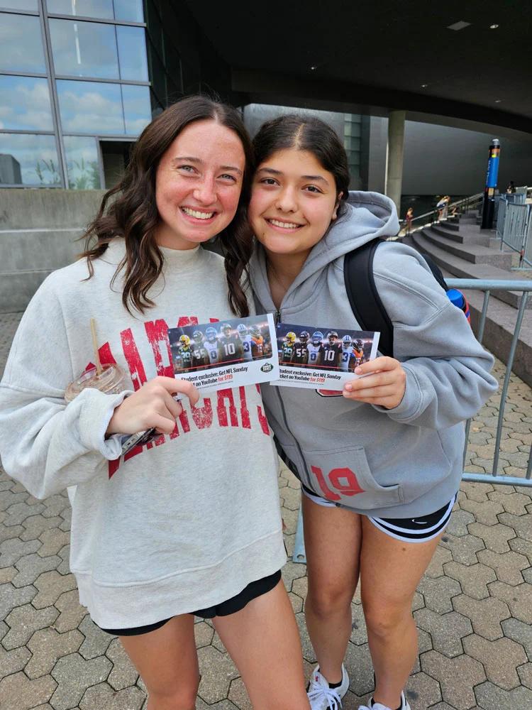 Image of two students holding YouTube NFL Sunday Ticket student offer cards outside a venue