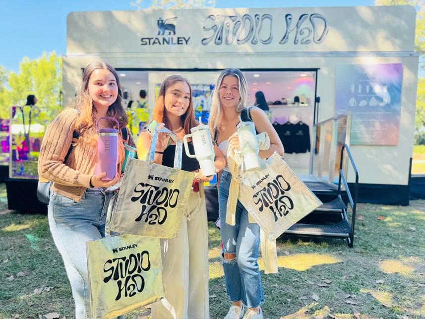 image of three women holding Stanley tumblers and Studio H2O tote bags outside the Stanley Studio H2O trailer