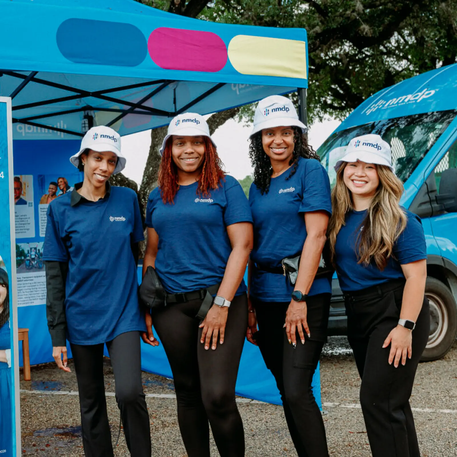 Image of four event ambassadors in branded apparel standing beside a mobile outreach activation booth