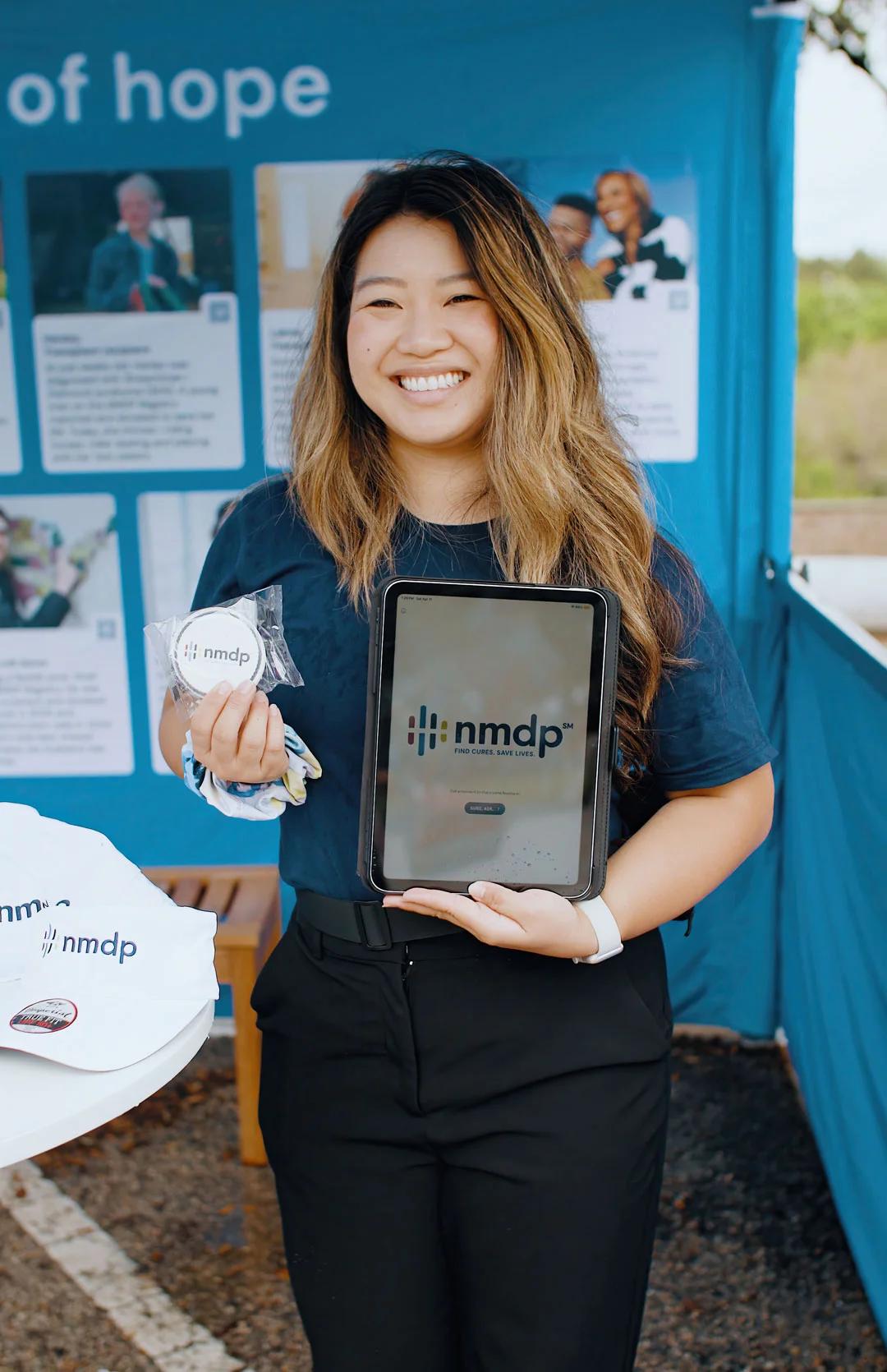 Image of an NMDP brand ambassador holding a tablet and promotional giveaway at an outreach event