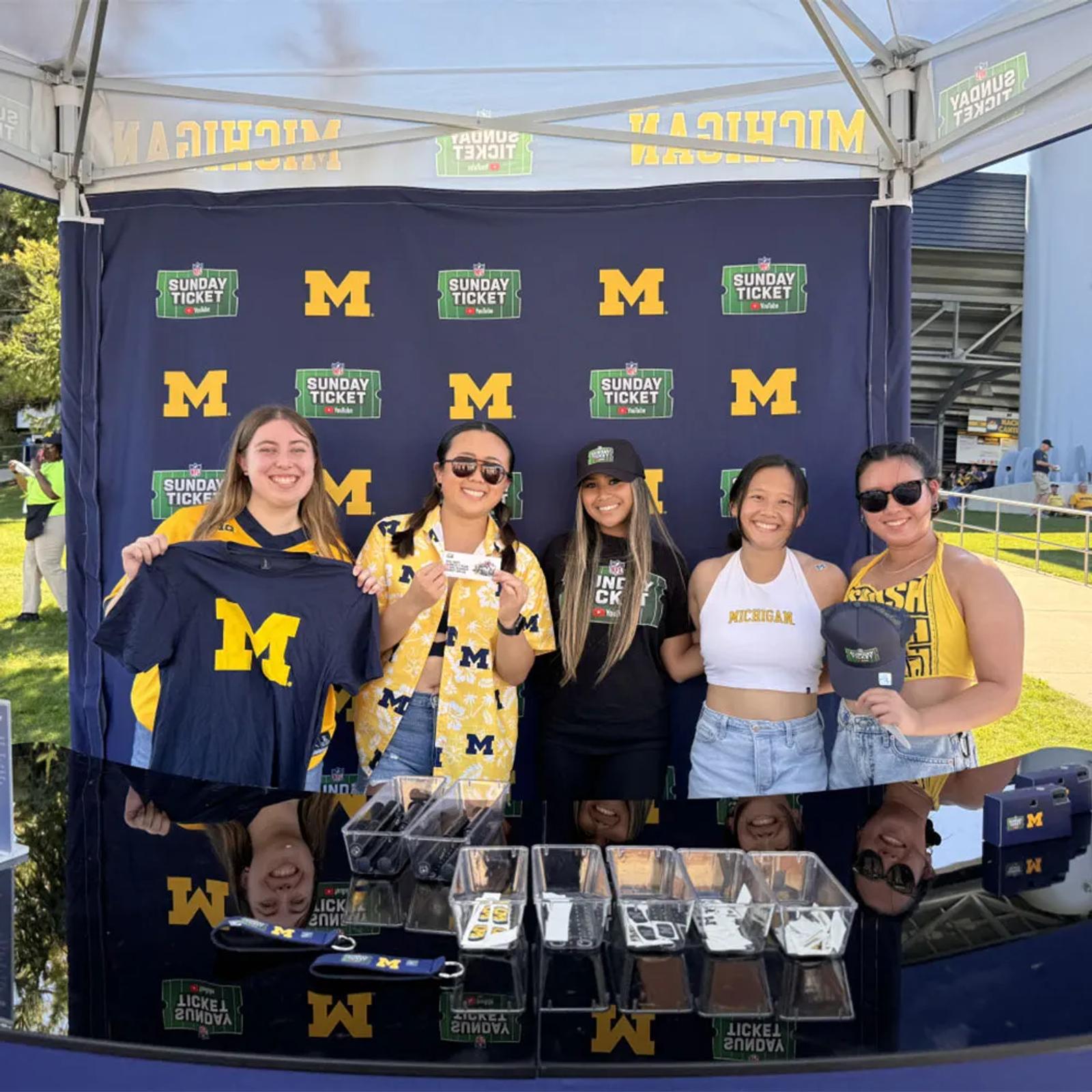Image of Michigan students holding giveaways in front of a YouTube NFL Sunday Ticket step-and-repeat backdrop