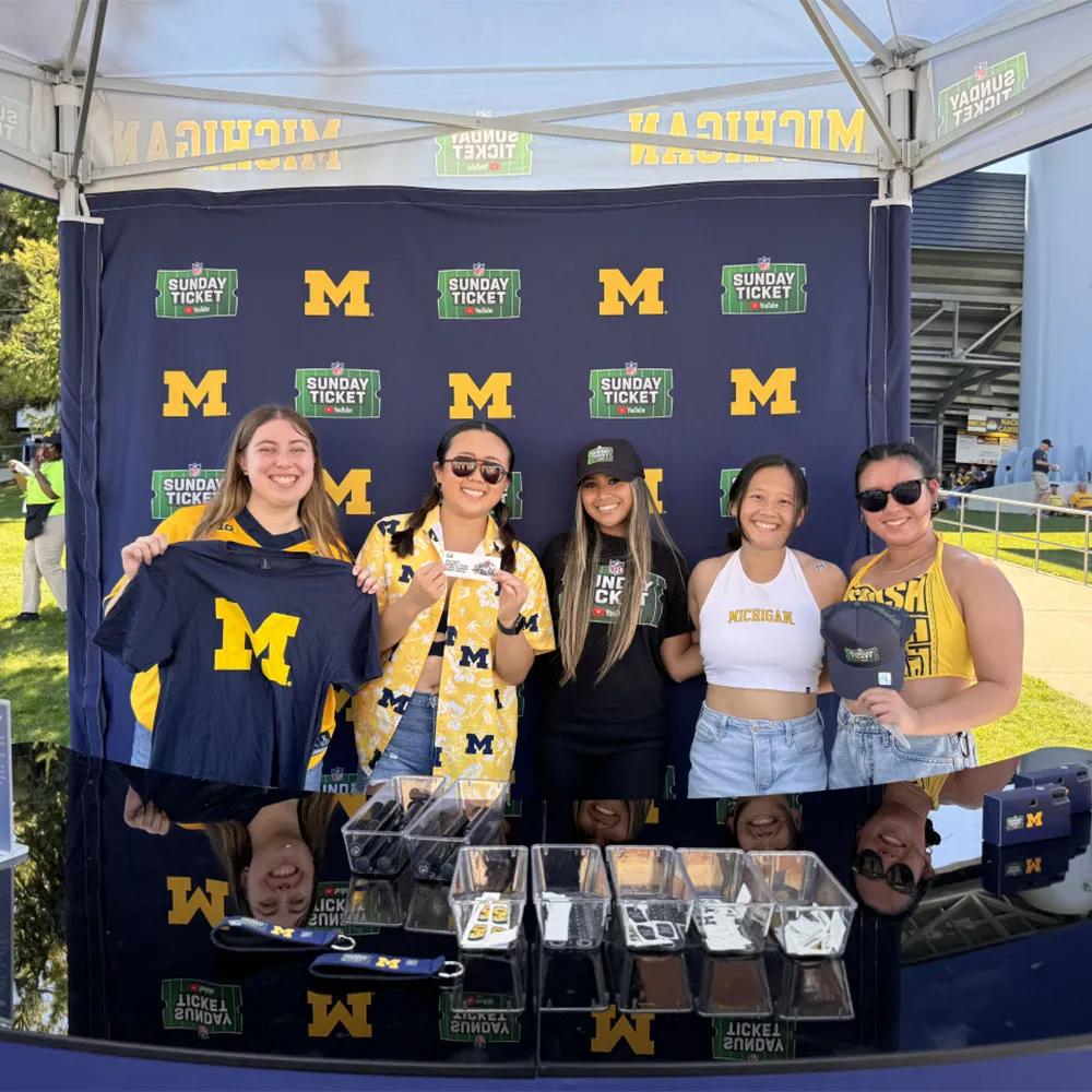 Image of Michigan students holding giveaways in front of a YouTube NFL Sunday Ticket step-and-repeat backdrop