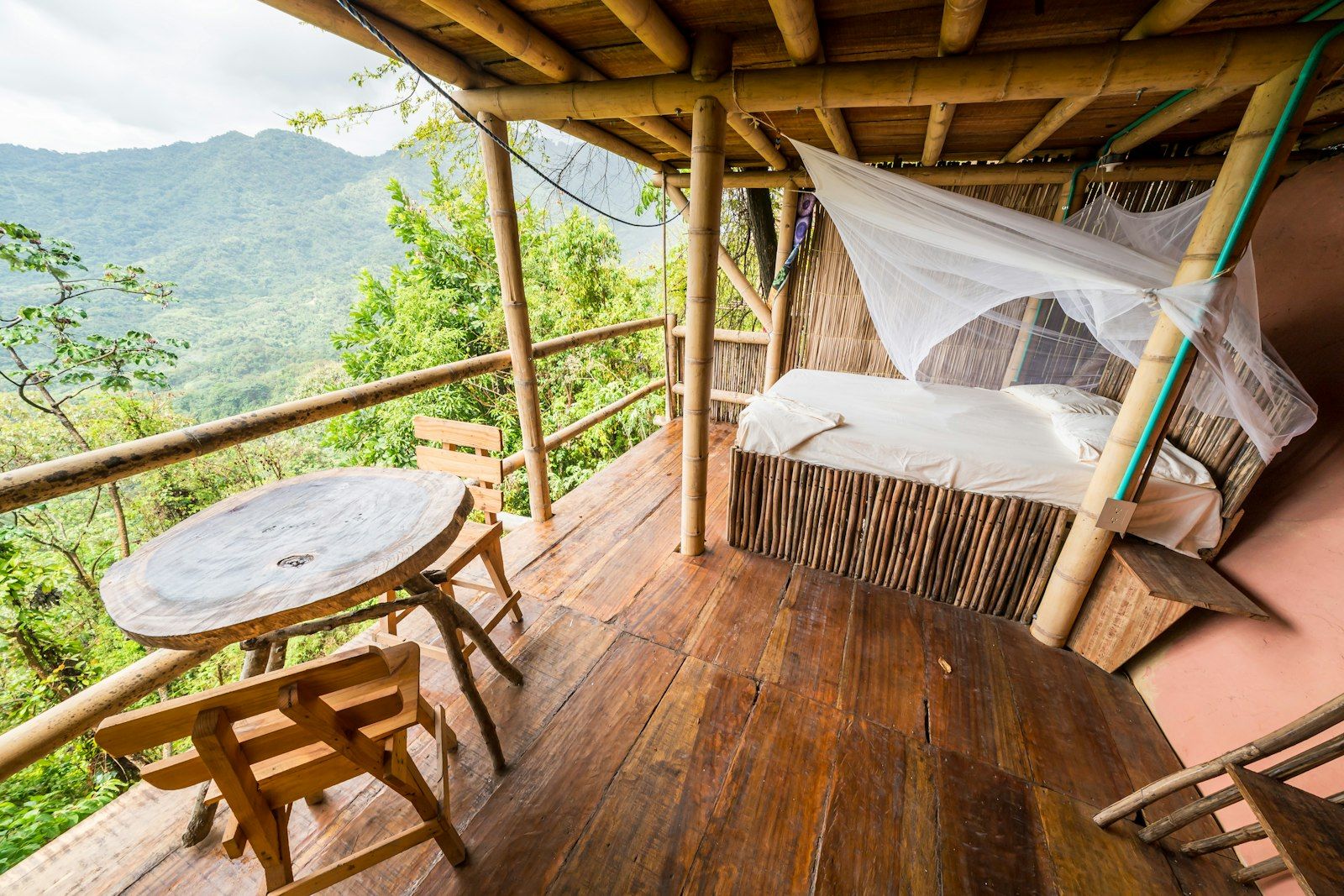 Bamboo hut with bed and table overlooking lush mountains