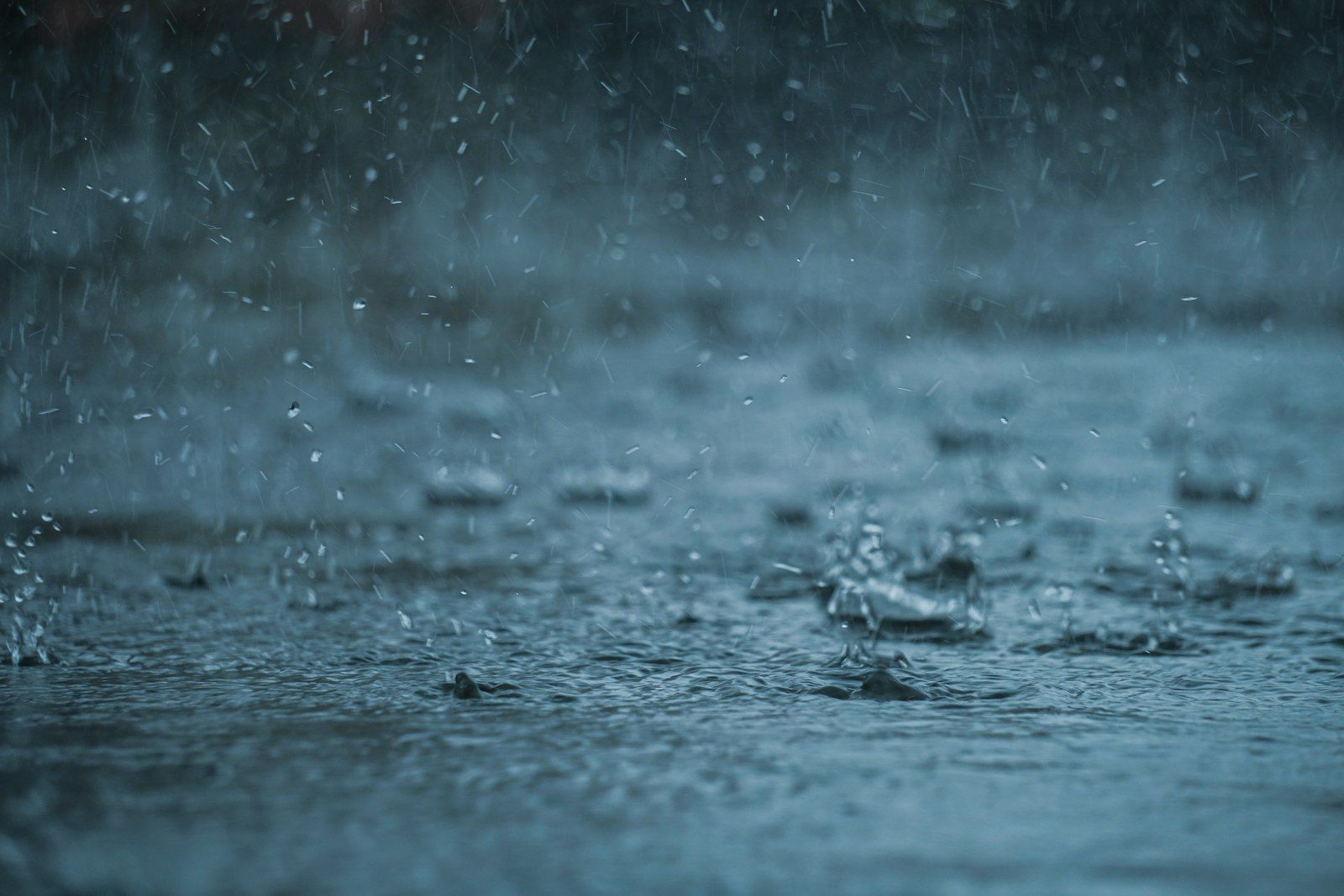 Heavy rain falling on a dark blue water surface with splashing droplets