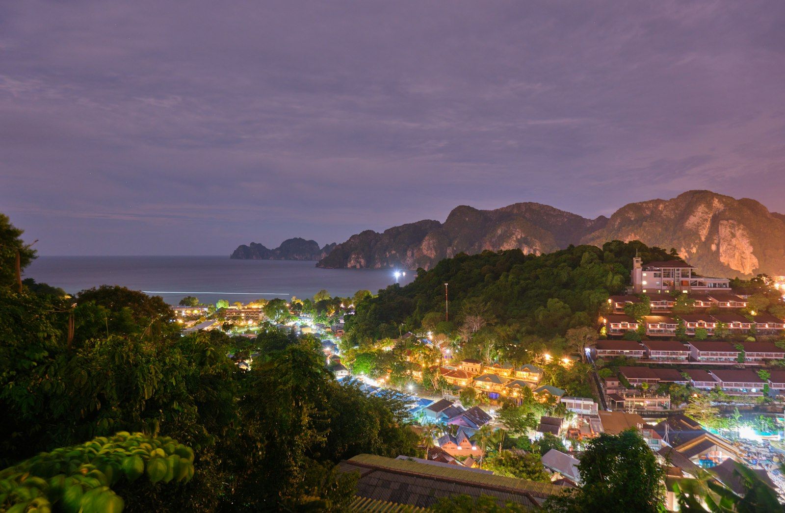 Tropical coastal town illuminated at night with distant mountains.
