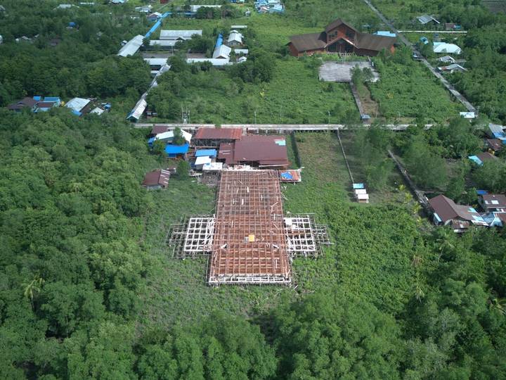 Lantai kayu mulai dipasang di atas rangka berbentuk salib, dengan kota Agats dan sungai di belakangnya, 24 Oktober 2025.