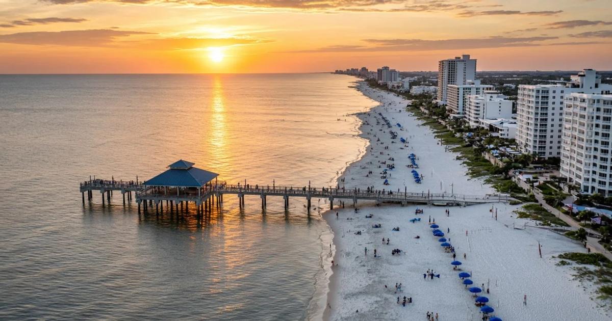 Aerial sunset view of Clearwater Beach with Pier 60, the public beach, and the beachfront condo and hotel towers along Gulf Boulevard.