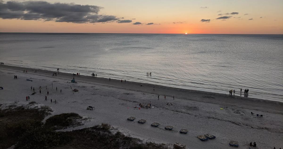 Sunset over the Gulf beach in Indian Shores, Florida, seen from above, with people walking on the dry sand