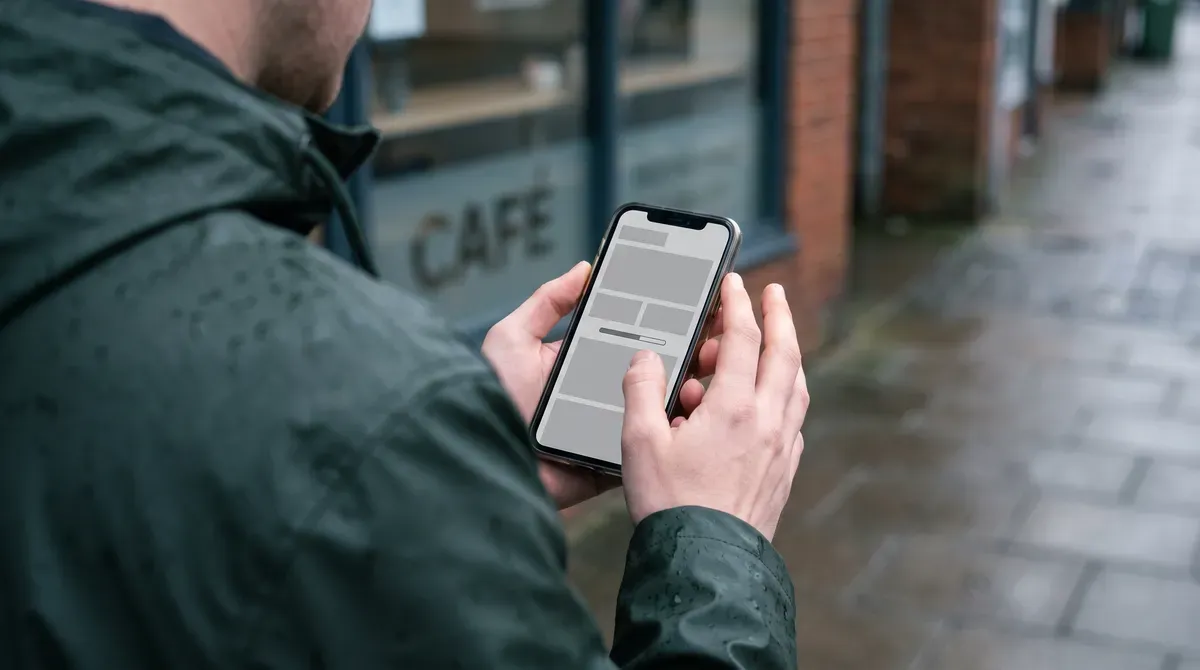 A business owner standing outside their own premises, waiting for their website to load on a phone