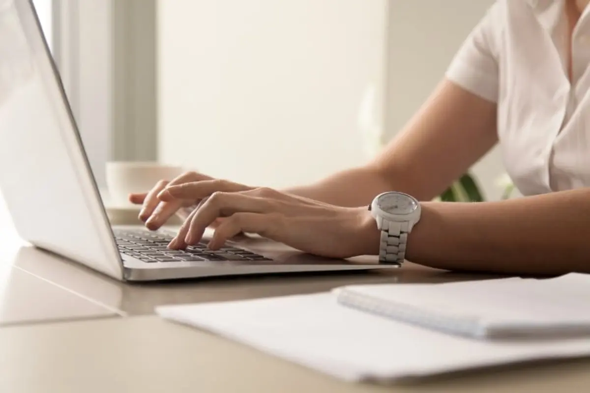 womans hands typing on laptop at workplace
