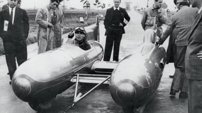 Coureur in racewagen met meerere mensen er omheen