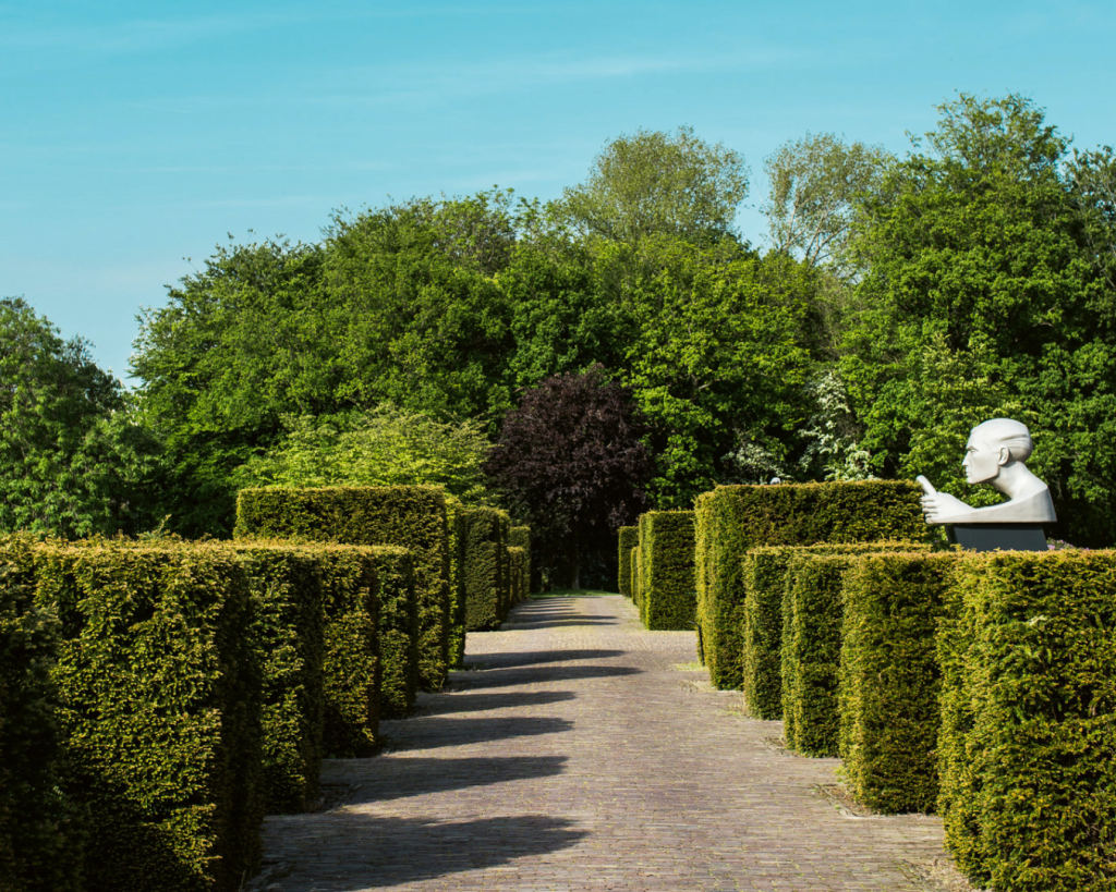 Groen tuinpad met vierkante bossage en een beeld van een hoofd aan de rechterkant