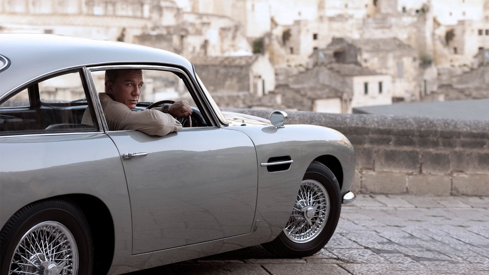 James Bond kijkt uit het raam van zijn Aston Martin DB5, oud stadje op de achtergond