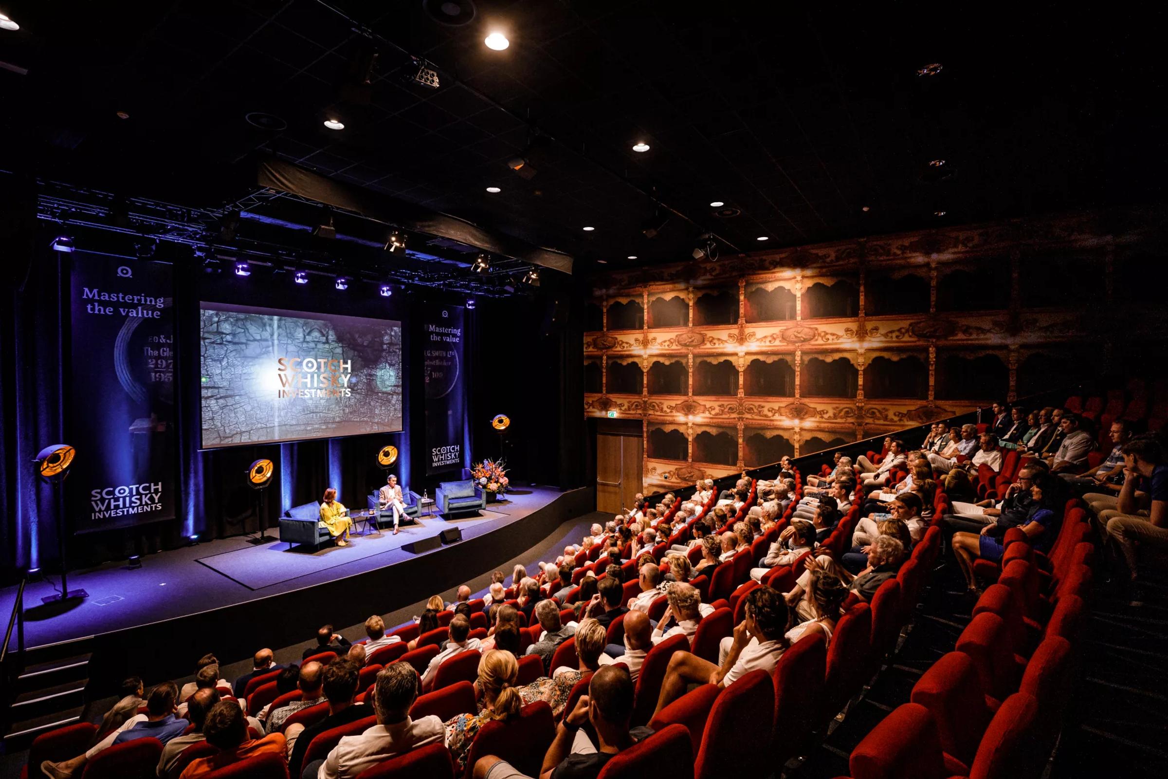 Een volle zaal waarin alle aandacht naar het podium gaat. De opstelling, techniek en sfeer zorgen voor een sterke beleving, waarbij elke spreker en elk moment helder overkomt op het publiek.