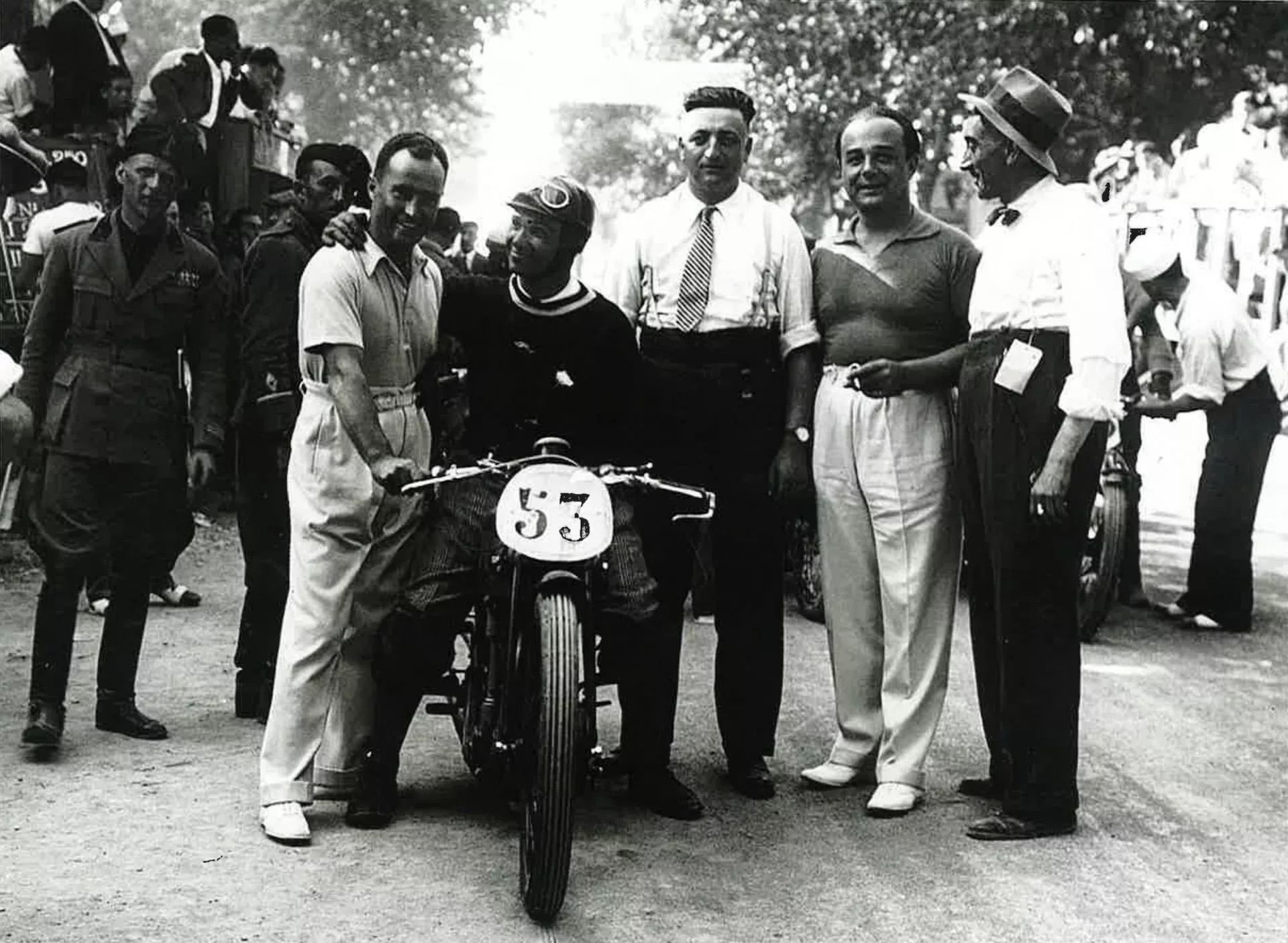 Man op een motor met rijtje mannen er naast