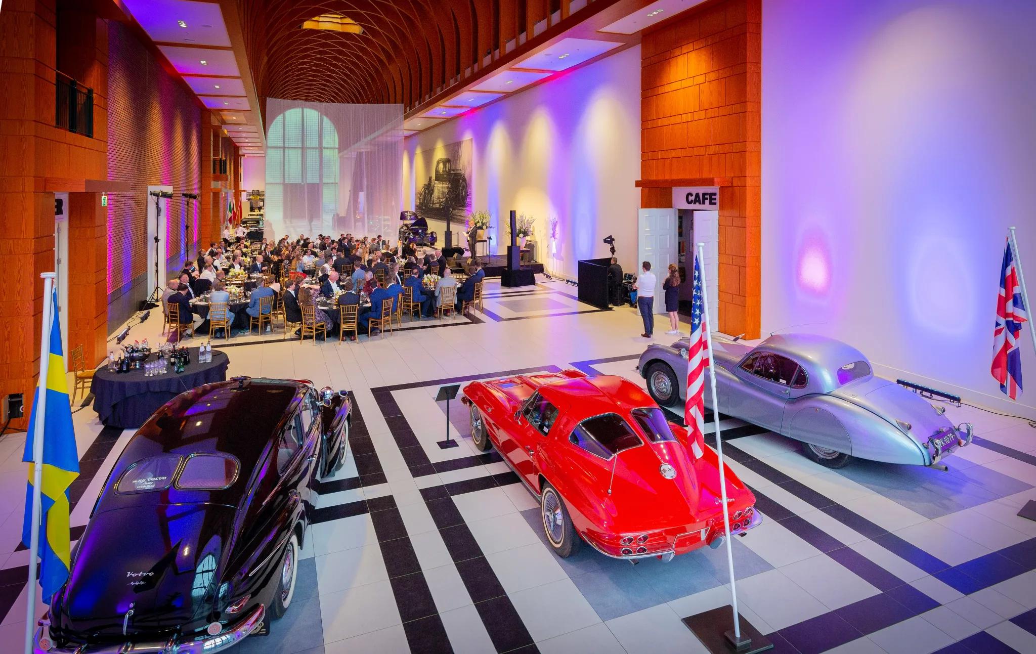 De great hall in het Louwman Museum met paars sfeerlicht en mensen aan grote ronde tafels