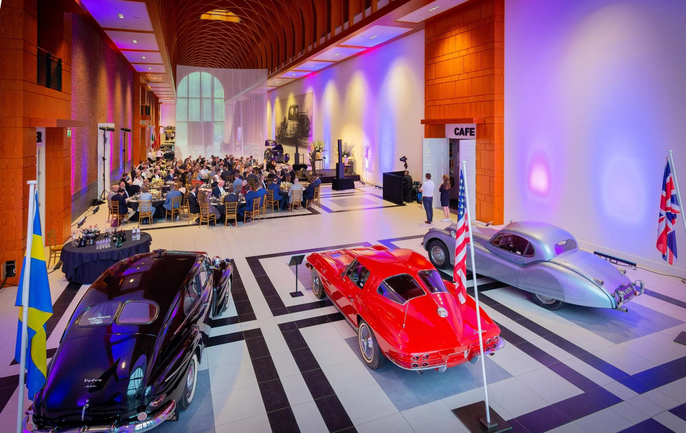 De great hall in het Louwman Museum met paars sfeerlicht en mensen aan grote ronde tafels