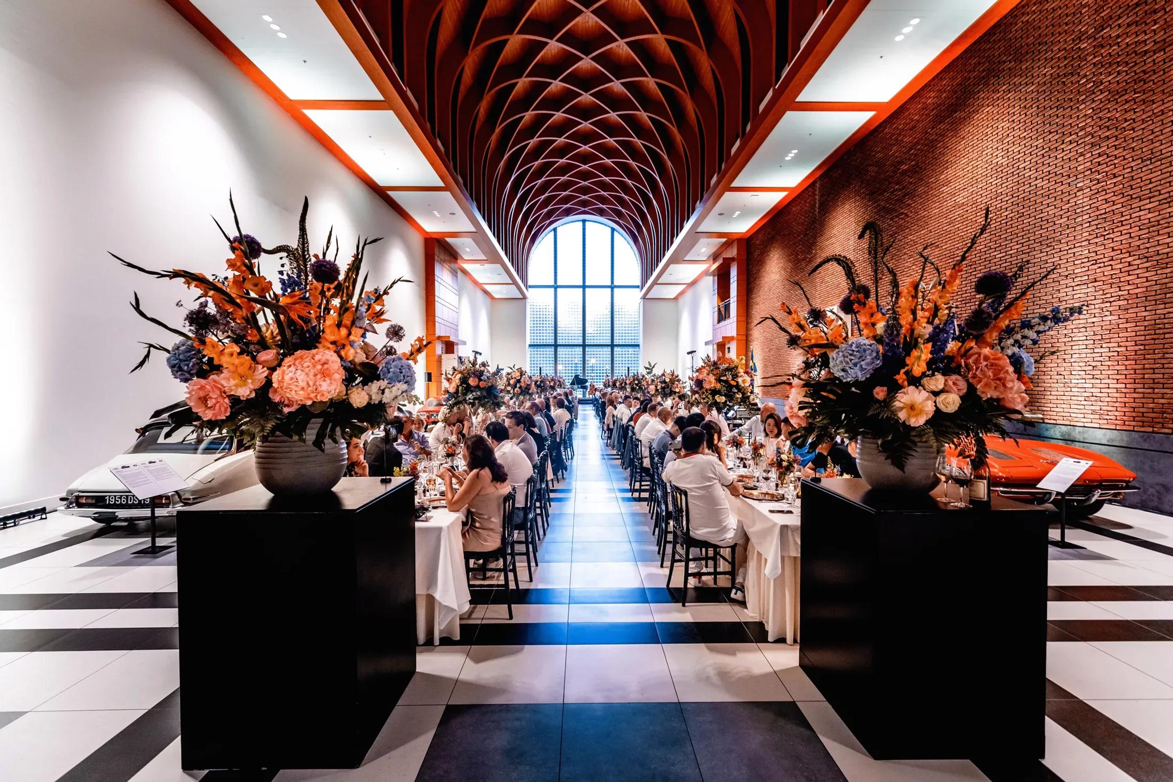 Twee bloemstukken en daarachter lange tafels in de great hall