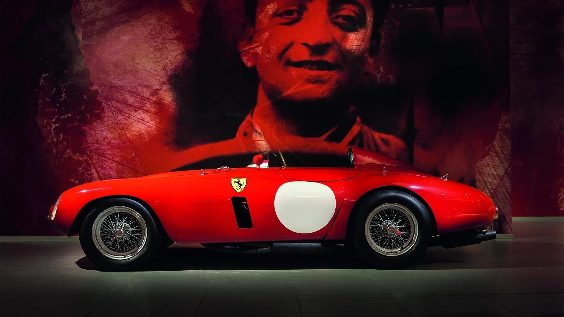 Rode Ferrari in donkere ruimte met grote foto van coureur op de achterwand