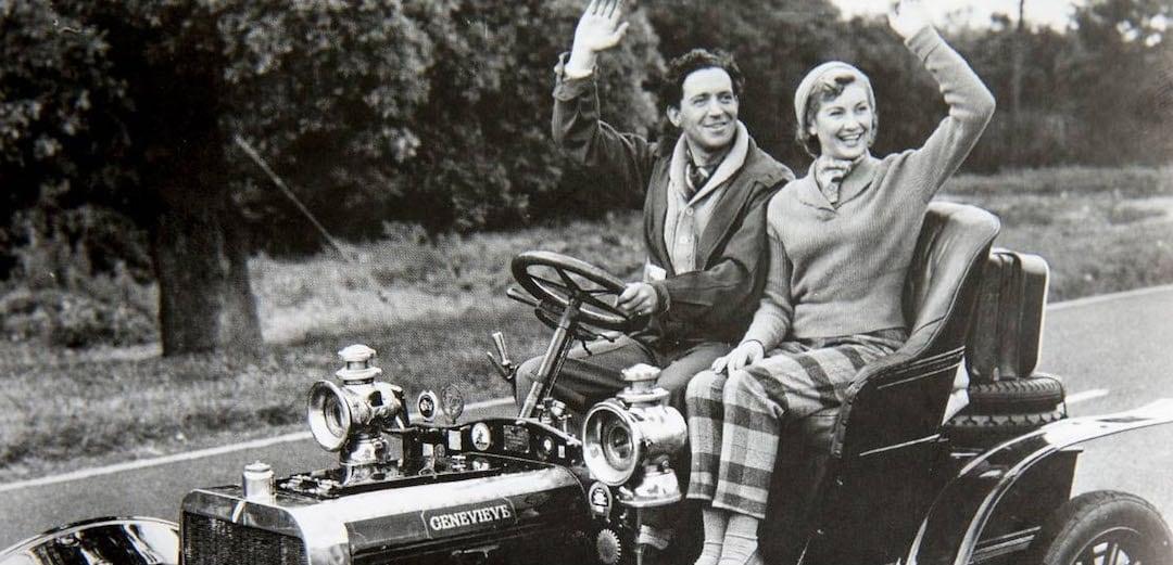 Photo en noir et blanc d un homme et d une femme conduisant et faisant signe dans une voiture ancienne nommee Genevieve