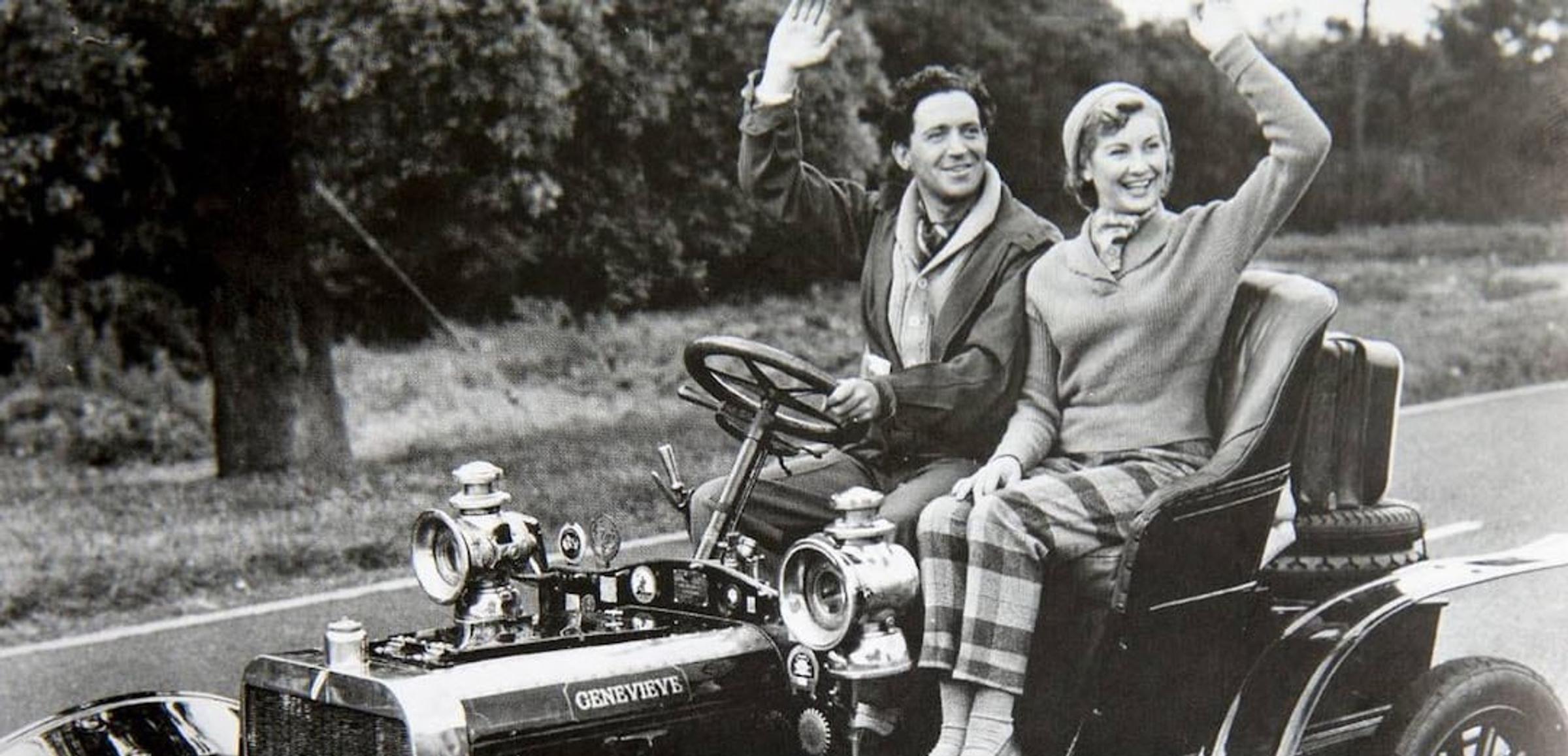 Zwart-wit foto van man en vrouw rijdend en zwaaiend in oldtimer met de naam 'Genevieve'